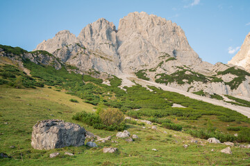 Fototapeta na wymiar Late afternoon under rocky cliff in Austrian Alps with Alpine meadow below.