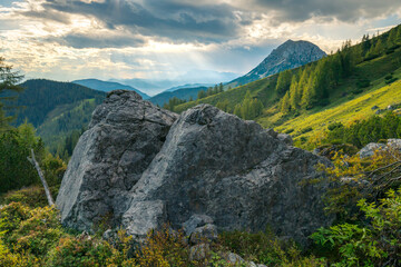 Dramatic sunset in the vast Alpine valley under the Hoher Dachstein massif on a summer day with two big boulders in the front. Last light on Alpine meadows.