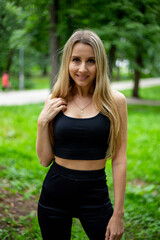 Fototapeta premium Young beautiful sporty blonde woman in a black T-shirt and in black tight sports shorts in good shape posing in front of green trees