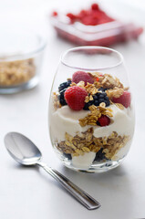A yogurt parfait with raspberries, blackberries and granola sit atop a white marble table top.