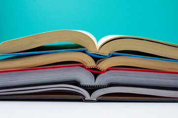 A stack of open books sits in front of a teal blue background.
