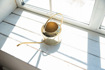 a yellow brass watering can with a long spout on a white windowsill. overexposed frame