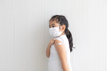 Asian cute girl wearing face mask showing vaccinated arm. Covid-19 Vaccination concept.