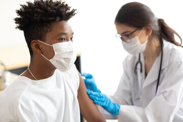asian woman doctor holding syringe and injection vaccine shot to black male patient. Young african...
