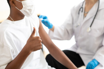 caucasian woman doctor holding syringe and injection vaccine shot to black male patient. Young african american man sitting and getting vaccinated against coronavirus in hospital