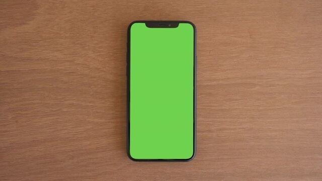 Smartphone place on wood table, Green screen telephone, Close up display mobile phone with mock up, Chroma key monitor, Close-up the cell phone on brown desktop, Mockup smartphone, Zoom top view.     