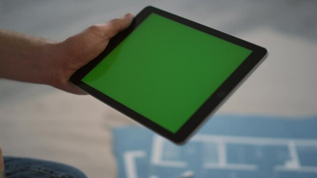 Unknown man showing green screen to camera. Guy using tablet for design indoors.