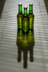 Three green glass beer bottles in the shade of the blinds.