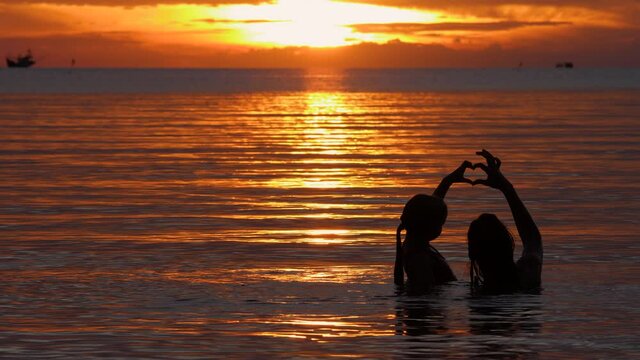 Mother and child daughter swim on wave water surface on sunset background. Friendship, love and happy family forever on summer vacation