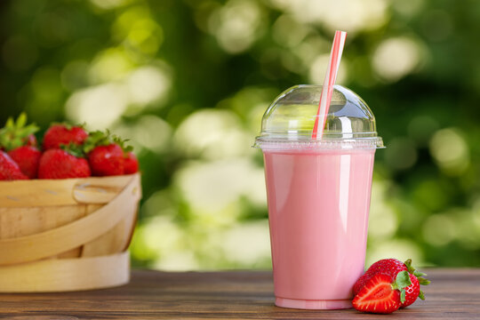 strawberry smoothie in disposable plastic glass on wooden table