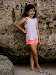 Young girl standing near the rock. Happy childhood. Spending time on the beach. Girl wearing shorts. Vacation in Asia. Pandawa beach, Bali, Indonesia