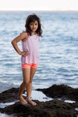 Young girl standing on the rock near the ocean enjoying nature. Happy childhood. Spending time on the beach. Vacation in Asia. Pandawa beach, Bali, Indonesia