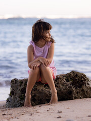 Young girl sitting on the rock near the ocean enjoying nature. Happy childhood. Spending time on the beach. Vacation in Asia. Pandawa beach, Bali, Indonesia