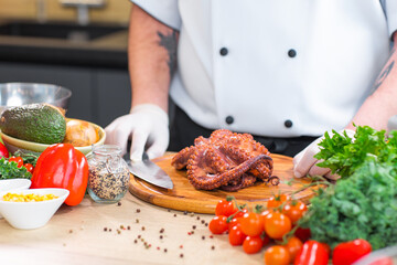 Young chef is cutting octopus in a modern kitchen. The man prepares food at home. Cooking healthy and tasty food.