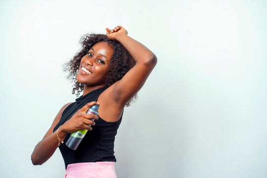 image of beautiful african lady with a cosmetic product, pointing at the armpit with a raised arm- indoor beauty concept