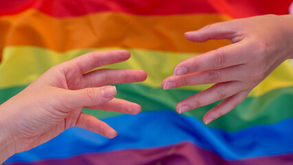 Parody of the mural Creation of Adam on the background of the LGBT flag during the celebration of the month of dignity, Bisexuality Day or National Coming Out Day. Female hands of lesbians