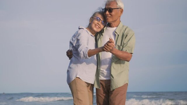 Happy Asian senior man and woman couple smile dancing resting relax on the beach honeymoon family sunny day, Romantic elderly enjoy travel summer vacation, plan life insurance at retirement couple