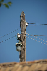 Power lines on an old wooden pole with street lighting against the blue sky in the day