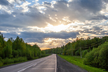 Country road with markings in the middle of the forest. Path and forward movement in the sun. Beautiful, green forest in the spring at sunset. Concept for success in the future goal and passing time