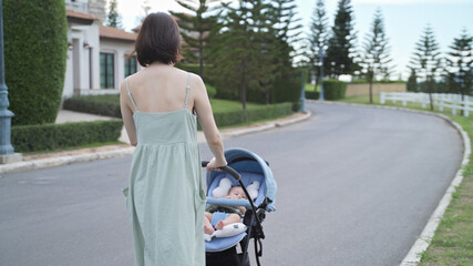 asian woman mother walking outdoor with baby infant in baby stroller around neighborhood street village in evening. pushchair buggy walk relaxation from home to garden. happy smile family.