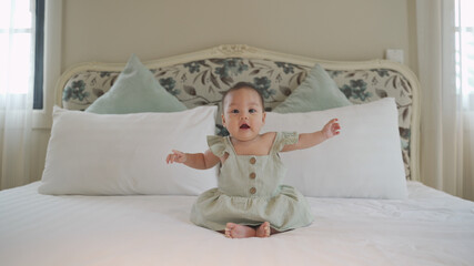 portrait of lovely asian baby infant 6 months learning to sit balance on bed. baby sitting skill development. happy smile baby self playing at home and delight.