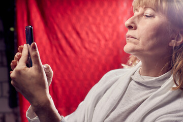 Obraz premium Portrait of a middle-aged woman with cell phone on a red background. Unprofessional female model doing selfie in the room or in the Studio