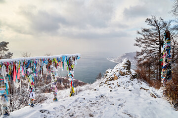 Buddhist multicolored wish ribbons at a height in the mountains above Lake Baikal in Russia. High landscape with Fencing with colored ribbons on a cliff with trees