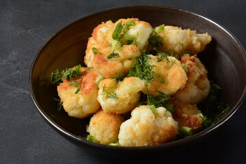 Fried cauliflower florets in batter on a black plate. Coated fried cauliflower