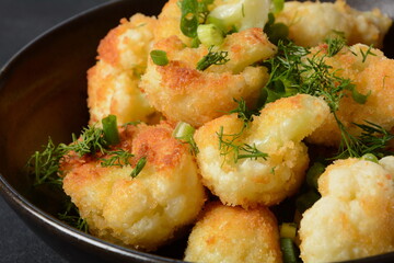 Fried cauliflower florets in batter on a black plate. Coated fried cauliflower