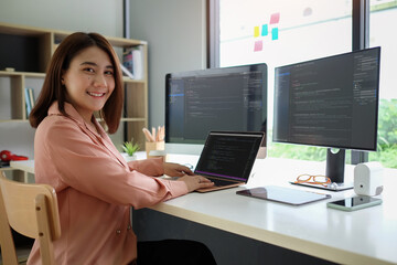Young female programmer working on project in modern office and smiling to camera.