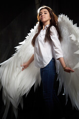 Beautiful girl with long hair posing in studio on a black background with angel white wings