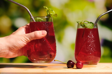 Summer drinks concept. Female hand with glass of cherry juice on summer natural background.