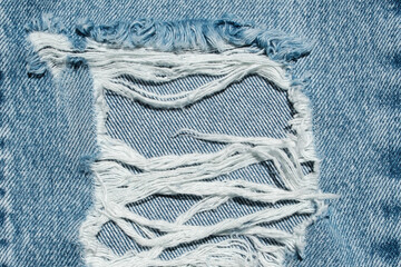 Hole and Threads on Denim Jeans. Ripped Destroyed Torn Blue jeans background. Close up blue jean...