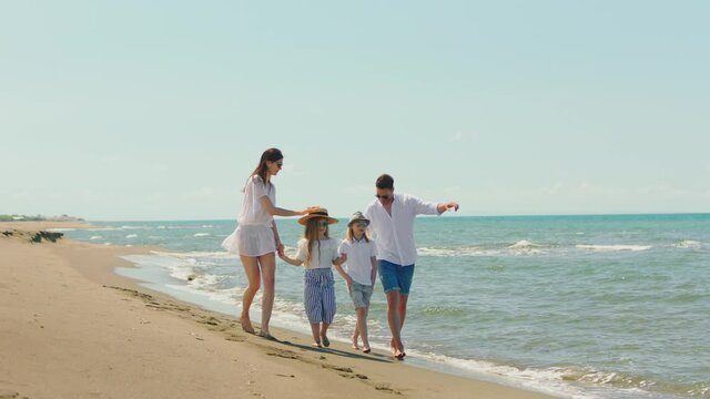 Young family walking on beach along coast. Woman putting straw hat on daughter's head. Sunny summer day at seaside.