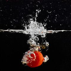 Fresh red tomato falling into water with water splash and air bubbles isolated on black background.