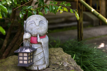 寺の片隅で赤いマフラーをして灯明を持つ笑顔の地蔵