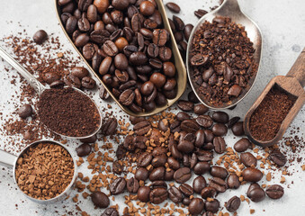 Freeze dried instant coffee granules with beans and ground coffee in various spoons and scoops on white background.