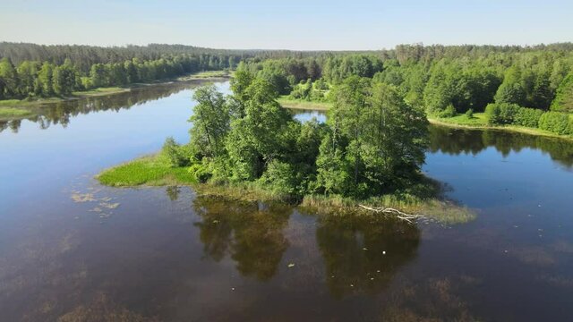 Top view of a lake in the forest with a small island,green trees around and in the midle of the lake water with reflecting sun rays