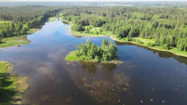 Top view of a lake in the forest with a small island,green trees around and in the midle of the lake water with reflecting sun rays