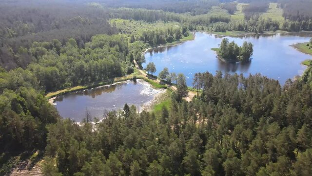 Top view of a lake in the forest with a small island,green trees around and in the midle of the lake water with reflecting sun rays