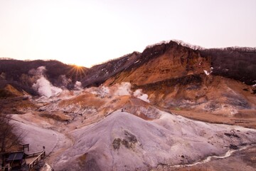 Sunrise at Jigokudani or Hell Valley in the town of Noboribetsu Onsen Hokkaido, Japan, hot steam vents, sulfurous streams. The man is standing on the wooden bridge which show a perspective view.