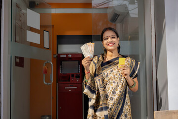 A RURAL WOMAN HAPPILY POSING WITH ATM CARD AND MONEY IN FRONT OF AN ATM