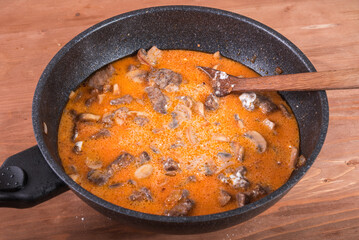Cooking classic beef stroganoff with mushrooms and sauce in a large skillet