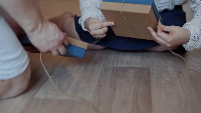 Caucasian man and woman at home on the floor are tying boxes with gifts with rope twine. Preparation for the holiday.
