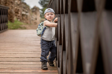 Two year old Caucasian boy posing leaning against a wooden bridge railing.