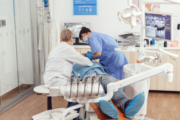 Senior dentist doctor and nurse preparing patient for removing crowns. Medic orthodontist wearing...