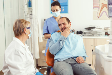 Obraz premium Stomatologist doctor talking to man patient with toothache sitting on dental chair preparing for medical examination. Dentists team working in stomatology hospital clinic office