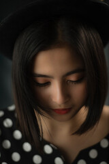 Young Asian woman wearing polka dot dress and pork-pie hat against dark grey background