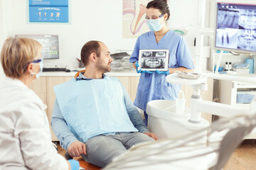 Obraz premium Medical nurse showing on tablet teeth x-ray showing it with patient. Dentist senior doctor and nurse working together in modern stomatological clinic, explaining treatment to man patient