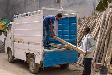 TWO WORKERS TOGETHER UNLOADING A TRUCK WITH WOODEN POLES